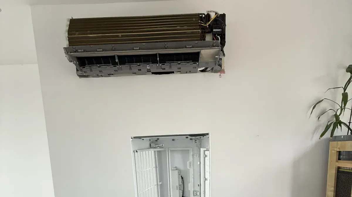 Technicien SaniClim+ effectuant le déblocage du drain d'évacuation d'une thermopompe murale afin d'éliminer un blocage et prévenir les fuites d'eau.